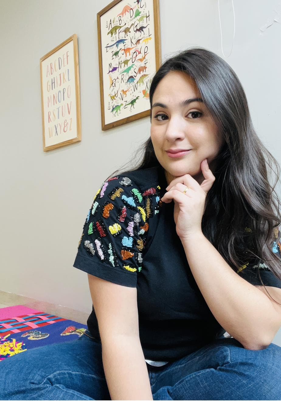 Daniella sorrindo no consultório infantil, sentada no chão com a mão no queixo